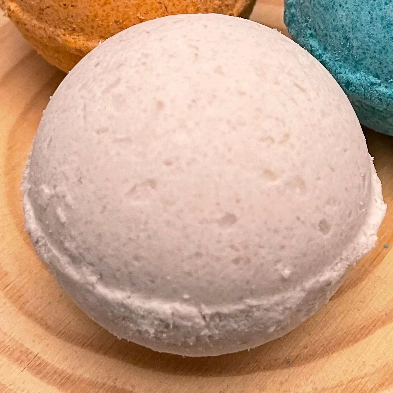 White bath bomb on wooden surface with orange and blue bath bombs nearby