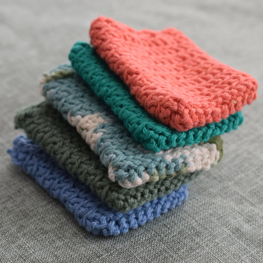 Stack of colorful handmade crochet dishcloths on a gray fabric surface