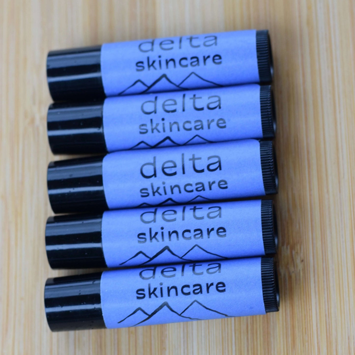 Five Delta Skincare lip balms on a wooden surface