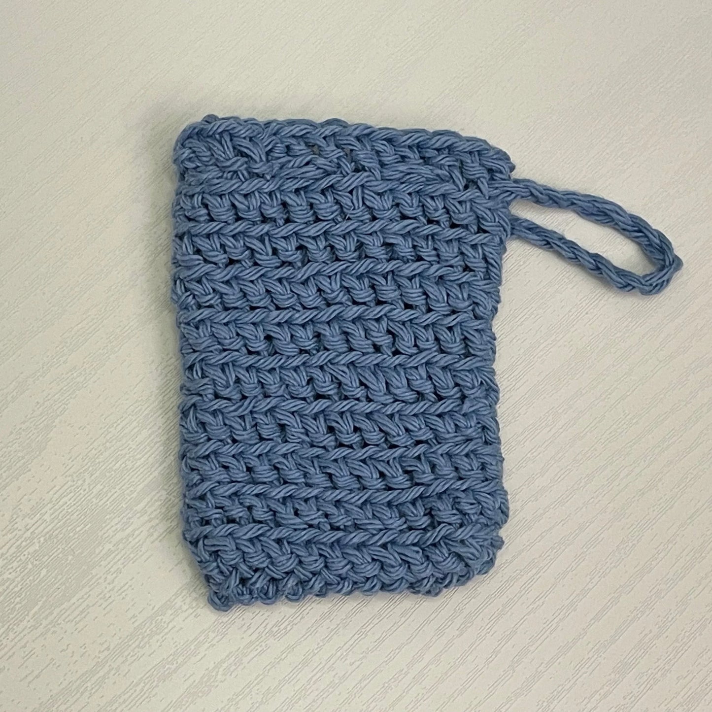 Handmade blue crochet soap saver pouch with loop on light wood surface