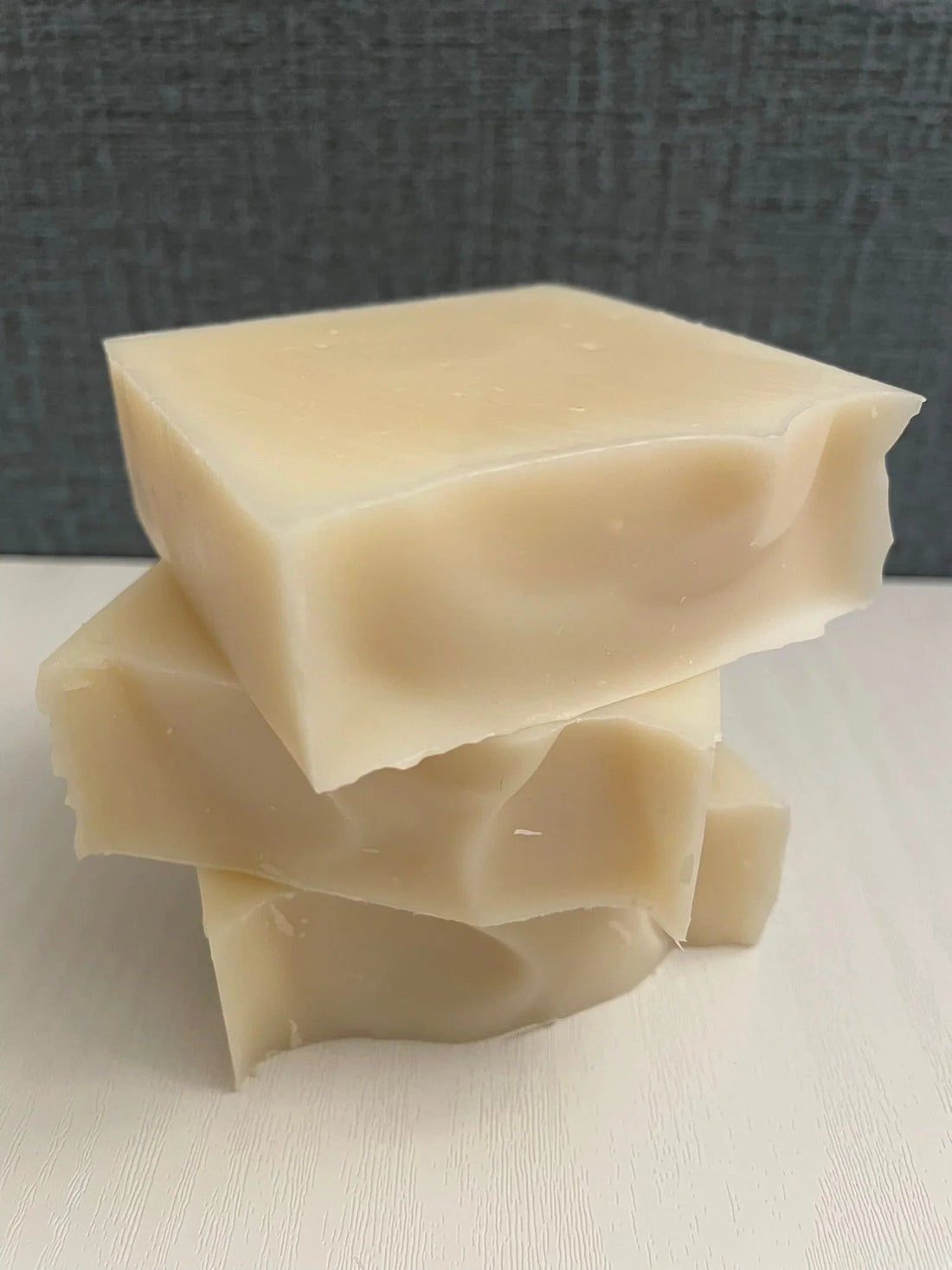 Three natural handmade soap bars stacked on white surface with textured gray background