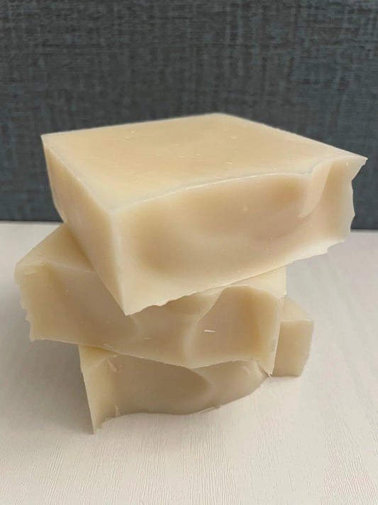 Three natural handmade soap bars stacked on white surface with textured gray background