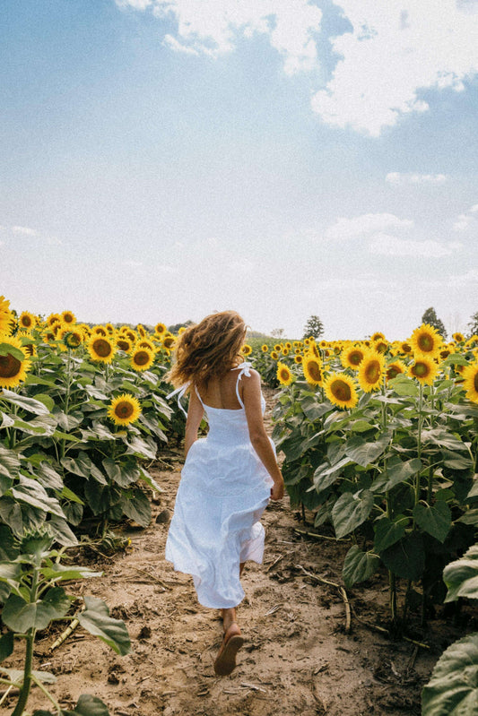 Woman in white dress walking through sunflower field under blue sky
