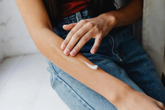 Person applying moisturizing cream to arm, close-up, skincare routine, casual jeans outfit