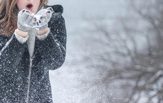 Woman in winter coat and gloves blowing snow outdoors in snowy weather