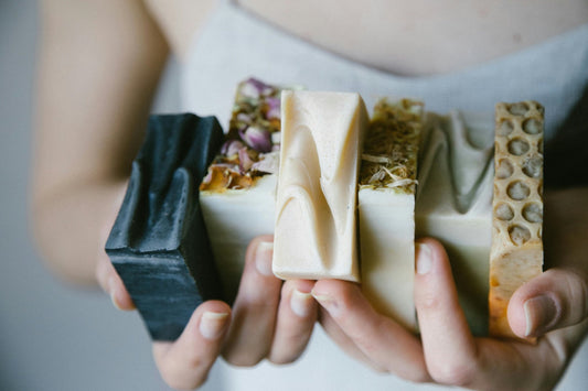 Hand holding assorted handmade natural soap bars with botanical toppings