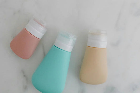 Three silicone travel bottles in pastel colors on a white marble surface