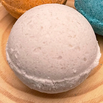 White bath bomb on wooden surface with orange and blue bath bombs nearby