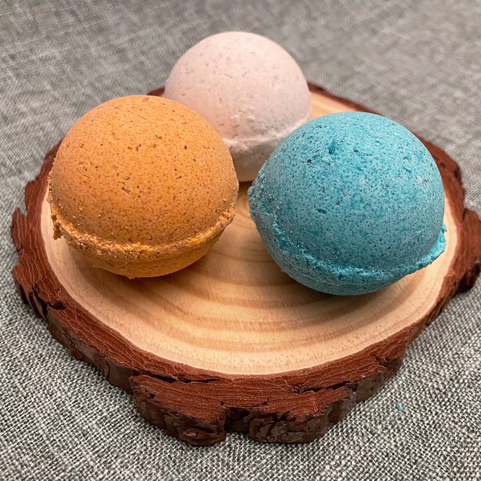 Three bath bombs in orange, white, and blue on a wooden coaster.