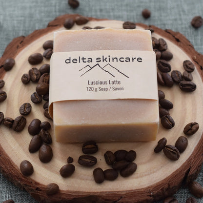 Delta Skincare Luscious Latte soap bar on wood slice, surrounded by coffee beans