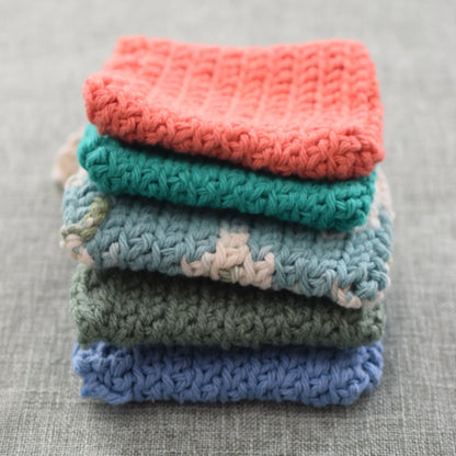 Stack of colorful hand-knit cotton dishcloths on a gray fabric surface