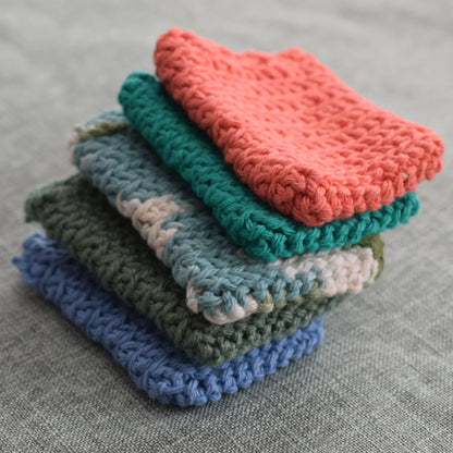 Stack of colorful handmade crochet dishcloths on a gray fabric surface