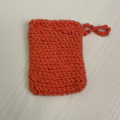 Handmade orange crochet soap saver pouch on a light wood surface