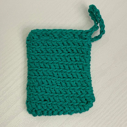 Handmade green crochet washcloth with a hanging loop on a light textured surface
