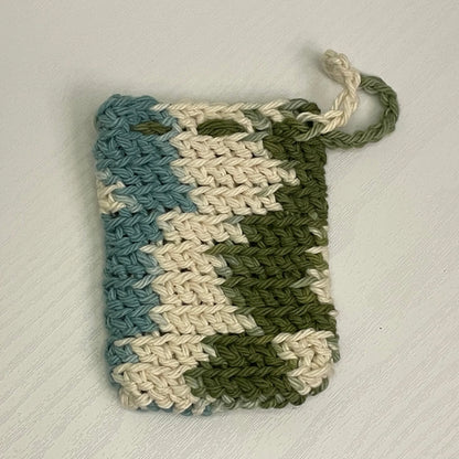 Handmade crochet soap saver pouch in blue, cream, and green on a white surface