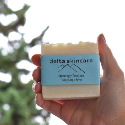 Hand holding Delta Skincare unscented soap bar with blue label outdoors